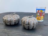 deux citrouilles en argent posées sur une table à côté d'un verre