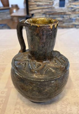un vase marron posé sur une table, avec un mur en pierre en arrière-plan