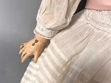 an antique doll wearing a white dress with a pink sash