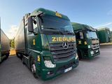 three green trucks are parked in a parking lot with a sky background