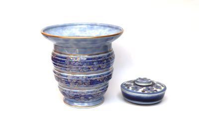 un vase bleu avec un couvercle posé à côté, sur une surface blanche