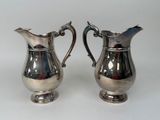 pair of silver plated pitchers with handles on a white surface