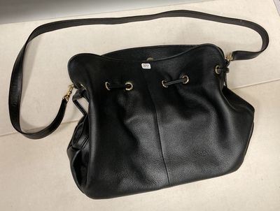 un sac à main en cuir noir posé sur une surface blanche, avec un ordinateur portable en arrière-plan