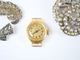 a gold watch, brooch, and other jewelry on a white surface