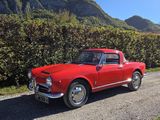 une vieille voiture rouge garée au bord d'un chemin de terre