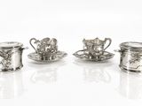 trois tasses à thé et soucoupes en argent sont posées sur une surface blanche