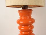 an orange table lamp with a beige shade on it