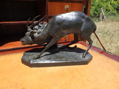statue représentant un cerf en pleine course, posée sur un socle en bois devant une bibliothèque