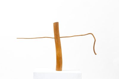 sculpture of a wooden cross on a white pedestal with a white background
