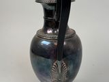 a silver vase with a black handle on a stand