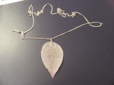 pendentif en feuille d'argent suspendu à une chaîne en argent sur un fond noir