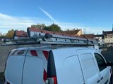 une camionnette blanche garée sur un parking, avec une échelle sur le toit