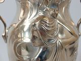 a silver vase with a woman on it on a table