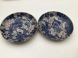 two blue and white plates with flowers on them on a table