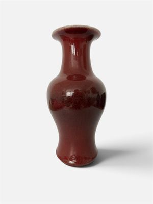 un vase rouge posé sur une surface blanche