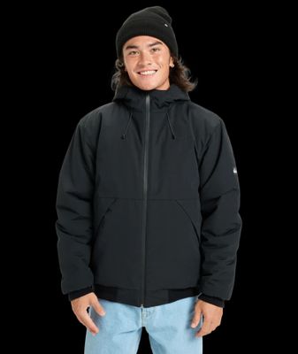un homme vêtu d'une veste noire et d'un jean, debout devant un fond noir