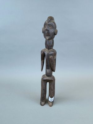 une vieille statue en bois représentant un homme assis sur un tabouret
