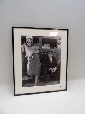 photographie en noir et blanc d'une femme appuyée contre une voiture, à côté d'un homme appuyé contre l'arrière de celle-ci