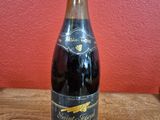 an empty bottle of wine sitting on a wooden table in front of a red wall