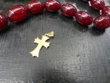 necklace with a gold cross and red beads on a black surface