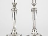 une paire de bougeoirs en argent posés sur des socles, sur fond blanc