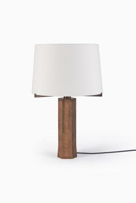 La lampe de table est en bois et est équipée d'un abat-jour blanc.