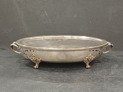 un plat ancien en argent avec des poignées, posé sur un fond noir