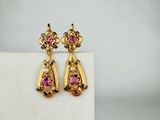 une photo représentant une paire de boucles d'oreilles roses et jaunes posées sur une surface blanche