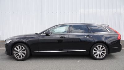 La Volvo break noire est garée devant un immeuble blanc.