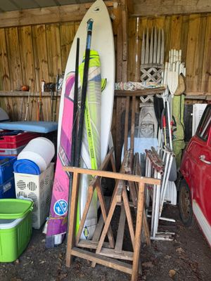 Plusieurs planches de surf sont empilées dans un garage, à côté d'une voiture rouge