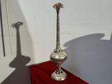 un vase en argent posé sur une table rouge, dont l'ombre se projette sur le mur