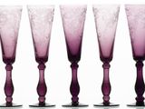 four purple wine glasses sitting next to each other on a white surface