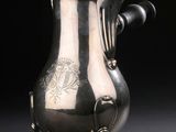 une cafetière ancienne en argent posée sur un socle, sur fond noir
