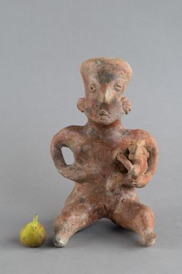 une vieille figurine représentant un homme tenant une poire, à côté d'une petite figurine représentant un homme
