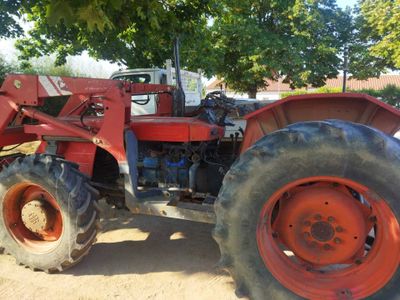 a red tractor parked in the dirt under a tree