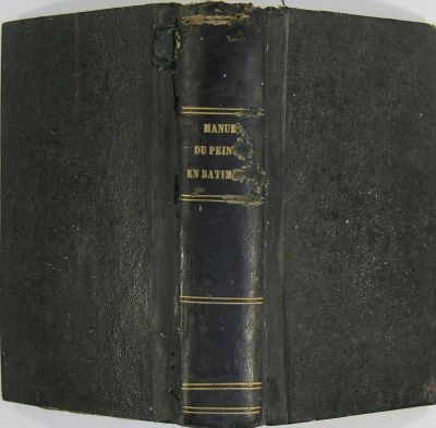 an old book with a black cover sitting on top of a table