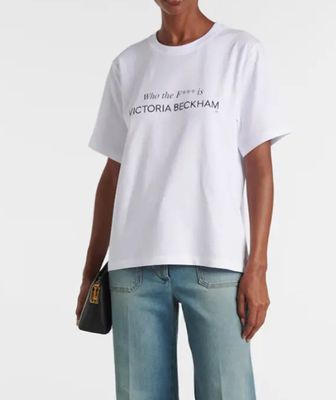 Une femme vêtue d'un t-shirt blanc et d'un jean se tient debout devant un fond blanc.