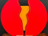 une sculpture rouge et jaune posée sur un socle en bois