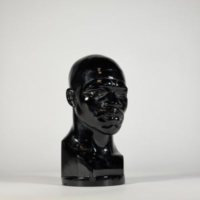 un gros plan sur une sculpture noire représentant la tête d'un homme, posée sur une surface blanche