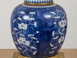 a blue and white vase with a gold base on a table