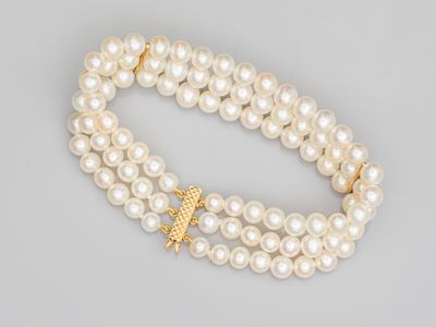 un gros plan sur un bracelet de perles blanches orné d'une breloque en forme d'étoile de mer en or