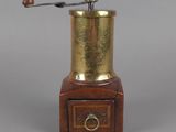un moulin à café ancien en laiton, posé sur un socle en bois muni d'un tiroir