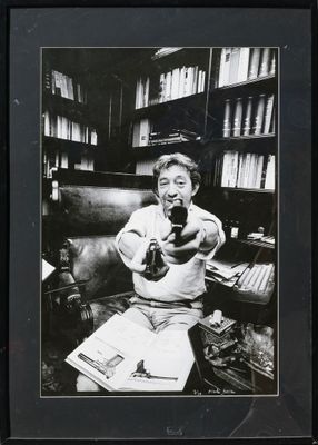black and white photograph of a man sitting on a couch holding a camera