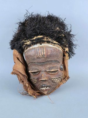 un gros plan d'un masque en bois aux cheveux noirs sur un fond blanc
