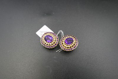 une paire de boucles d'oreilles violettes et dorées posées sur un fond noir