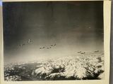 black and white photograph of a group of airplanes flying over snow covered mountains