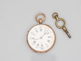 a close up of a pocket watch and a key on a table