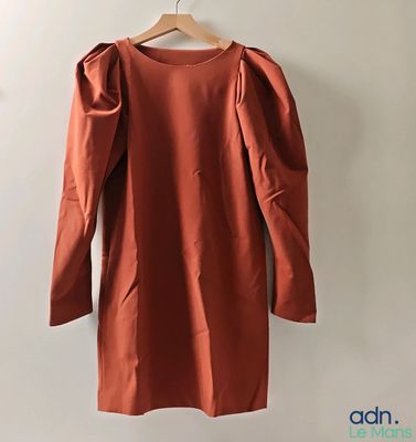 une robe orange suspendue à un cintre devant un mur blanc