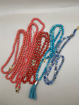 trois colliers de perles avec des pompons, posés sur un fond blanc