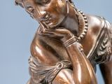bronze statue of a woman sitting on a rock with her hand on her chin